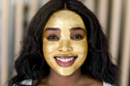 Cosmetic mask, beauty and skin care concept. Pretty charming African American lady with golden mask...