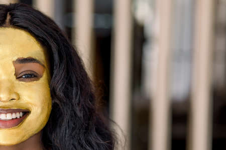 Cosmetic mask, beauty and skin care concept. Cropped image of charming African woman with golden mask on her face, posing to camera with smile, enjoying her facial treatment at home. Copy space.の写真素材