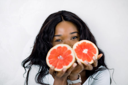 African American woman with long dark hair, smiling for camera and hiding half of her face with...