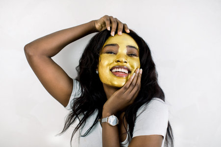 Cosmetic mask, beauty and skin care concept. Pretty charming African American lady with golden mask...
