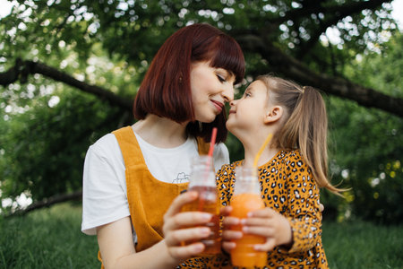Close up view of happy caucasian mother and her cheerful daughter drinking juice in summer day outdoor in green park. Vacation and mothers day concept.の写真素材