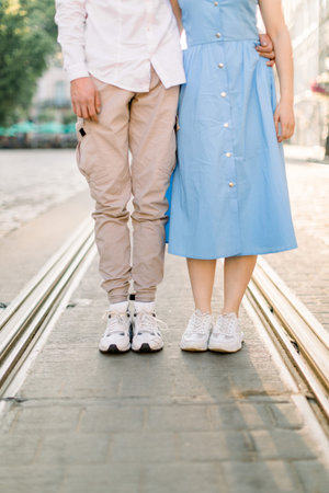 Cropped image of legs of lovely stylish young couple in love, woman in blue dress and man in beige...