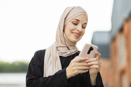 Portrait of beautiful muslim female in black clothes watching online story on mobile phone,...