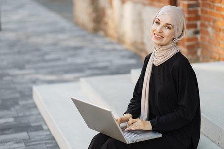Close up portrait of young Muslim Arab woman freelancer in hijab working on laptop sitting on...