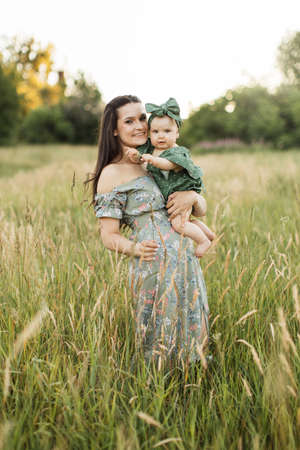 Cheerful young woman in green summer dress lifting up six month old baby girl while playing walking on field. Mother with daughter enjoying time spending together on fresh air.の写真素材
