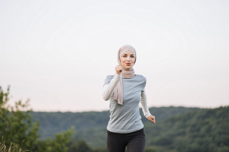 Jogging Arabic woman in hijab running in green park on beautiful summer day. Sport fitness model...