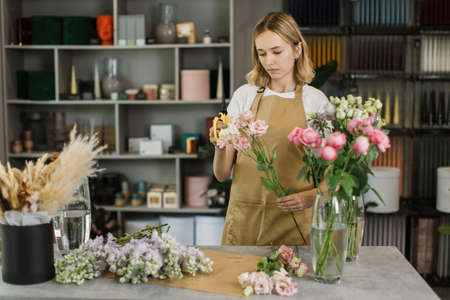 Woman florist at her own floral shop taking care of flowers. People, business, sale and floristry concept. Happy smiling florist woman making violet flower bunch at flower shopの写真素材