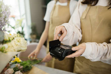 Close up view of hands of young florist female receiving discount card from regular customer and making payment at terminal in flower shop.の写真素材