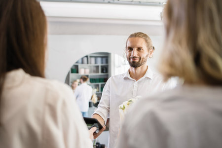 Attractive young bearded man shopping and paying with electronic credit card in his smartphone using app in flower shop.の写真素材