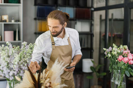 Small business. Male florist in flower shop. Floral design studio, making decorations and arrangements. Flowers delivery, creating order.の写真素材