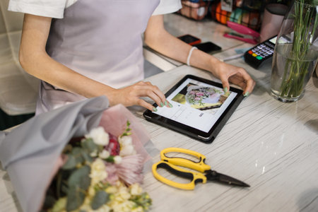 Close up hands of female wearing apron, working in flower shop. Pretty young female florist using...