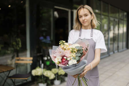 Portrait of smiling male florist standing in front of flower shops facade with wonderful bouquet of flowers. Small business.の写真素材