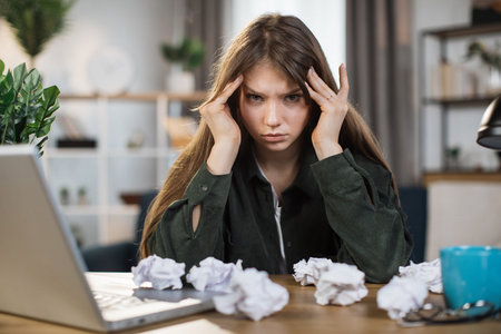Caucasian young woman stressed about work at home office and look at something on the laptop screen,...
