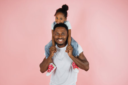Happy family. Portrait of cheerful african american man riding excited daughter on his shoulders,...