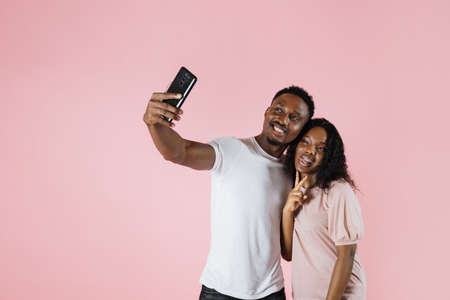 Joyful people using mobile phone to take selfies together in studio. Man and woman taking picture with smartphone and having fun in front of camera. Carefree couple feeling happy.の写真素材