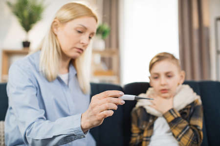 Close-up of moms hand, holding thermometer. Excited pretty mother comforting hugging her child, checking her sick teen sons temperature. Parenthood, disease, quarantine concept.の写真素材