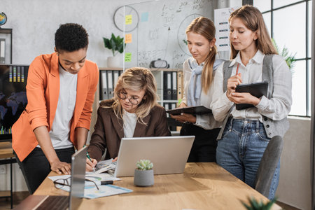 Teamwork, brainstorming in office. Diverse multiracial business people working together with laptop and tablet pc while their senior woman leader sign in report papers.の写真素材