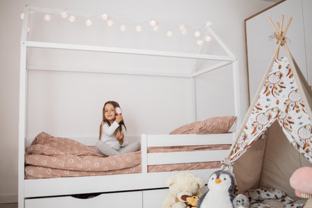 5 years old girl brushing her long hair in her bedroom in the morning. Funny little female child combing her hair. Happy baby sitting on the bed.の写真素材