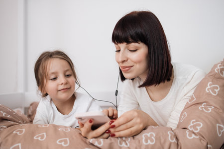 Close up of smiling mom and little daughter relax in cozy bed read funny interesting children book together, happy mother and small preschooler girl child enjoy fairytale rest in comfortable bedroomの写真素材