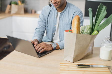 Cropped view of arabian businessman preparing healthy salad while work from home. Attractive handsome male feel happy, use laptop computer study, learn online before eating clean vegetables in kitchenの写真素材