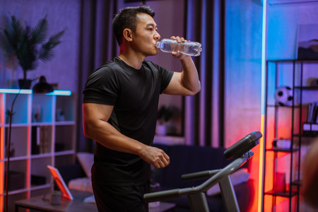 Attractive young sports asian man drinking water from bottle doing fitness exercise, running on...