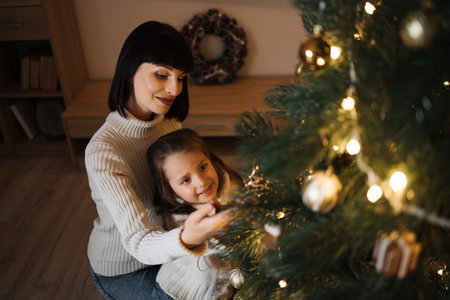 Mother and daughter decorating Christmas tree at home. Stylish interior of a childrens room. Scandinavian eco-style decor. New Year celebration. Christmas eve. Support joint time forwarding. Loveの写真素材