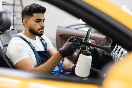 Professional chemical cleaning of interior of yellow luxury cabriolet car by air gun. Male bearded worker of auto service station, cleaning modern vehicle interior with tornado air gun.の写真素材