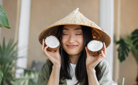 Fashion. Asian woman in summer clothes with coconut in tropical nature background. Beautiful smiling...