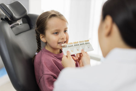 Tooth teeth tone palette. Stomatologist orthodontist dentist choosing selecting color of patient cute little preschool girl teeth for whitening at clinic.の写真素材
