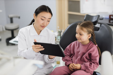 Medicine, pediatric dentistry and oral care concept. Female smiling asian dentist showing tablet pc...
