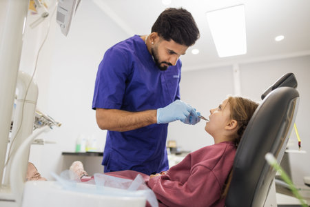 Beautiful smile with white teeth. Confident bearded dentist examines the oral cavity of a young beautiful girl through a magnifying glass in the dental office.の写真素材