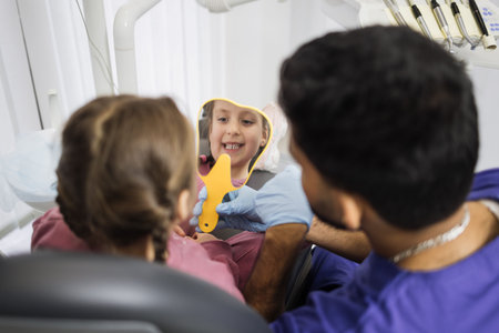 Happy cute little girl enjoying her beautiful toothy smile looking at mirror while young bearded...