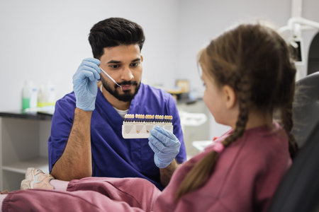 Visual method of subjective perception color of filling by a doctor. Young professional male dentist choosing color of filling from palette for little cute female child in light moderm dental clinic.の写真素材