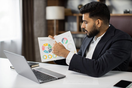 Serious marketing professional man in suit talking to client on video call, presenting paper graphic...