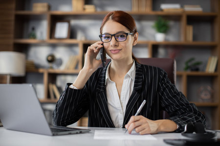 Business, technology, communication and people concept - happy smiling caucasian businesswoman sitting at desk with papers calling on phone at modern office.の写真素材
