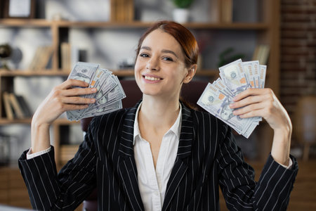 Portrait of happy young attractive female accountant holding cash banknotes, counting money at...