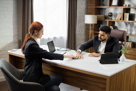 Young red hair businesswoman giving an illegal money or bribe money to her bearded business dealer in the office. Tribute, dirty money, bribe concept.の写真素材