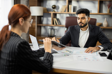 Focused young businessman signing agreement with skilled female lawyer. Concentrated financial advisor showing place for signature on paper contract document to male client at meeting in office.の写真素材
