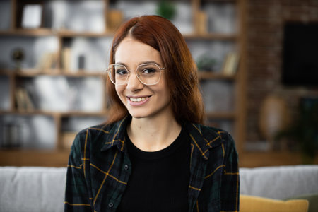 Close up portrait of happy red hair caucasian woman sit rest on comfortable couch in modern living room distance dreaming. Smiling young female renter or tenant relax on sofa at home, enjoy weekend.の写真素材