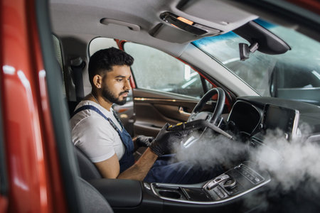 Auto cleaning service and detailing concept. Handsome young bearded man in blue uniform overalls...