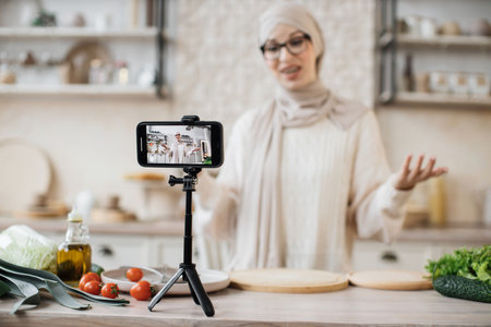 Excited muslim woman recording new video for her dieting and food blog on smartphone, standing in...
