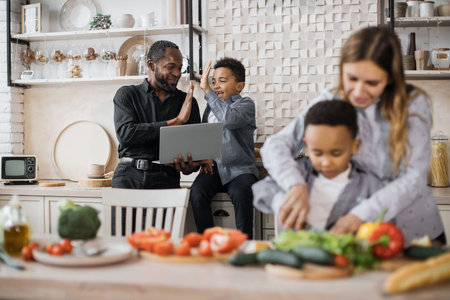 Focus on loving african father and small boy child finding recipe of holiday meal and giving high five. Happy mother teach little preschooler son chop vegetables preparing salad for lunch together.の写真素材