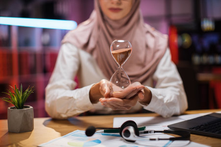 Focus on hands of confident businesswoman in hijab sitting at desk with modern laptop and holding...