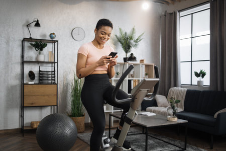 Portrait of young african female wearing sportswear writing message on her smartphone while working...