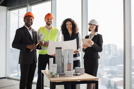 Happy multiracial architects, engineers and designers standing near skyscrapers buildings maquette during meeting at boardroom. Men and women colleagues leading meeting for architectural project.の写真素材
