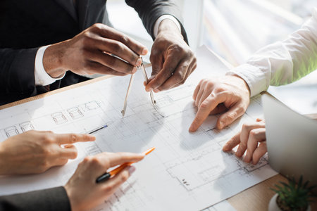 Close up of architects, engineers and designers sitting together at table and analysing blueprints....
