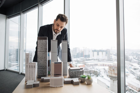 People, global business, company worker concept. Portrait of confident bearded businessman real estate agent in formal clothes, looking at building complex prototype project of 3d city model at tableの写真素材