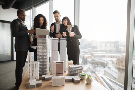 Close up of model of real estate project. Team of diverse multiethnic businesspeople working with financial reports using laptop at open space office with white walls and panoramic windows.の写真素材