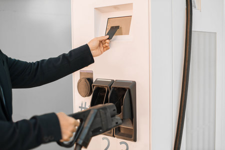 Close up of stylish asian entrepreneur taking power cord at charging station and paying with credit card for energy. Wireless technology in city infrastructure.の写真素材