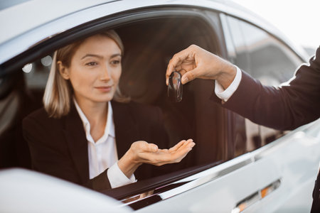 Close up of male seller giving keys from white modern car to happy female owner in formal wear....